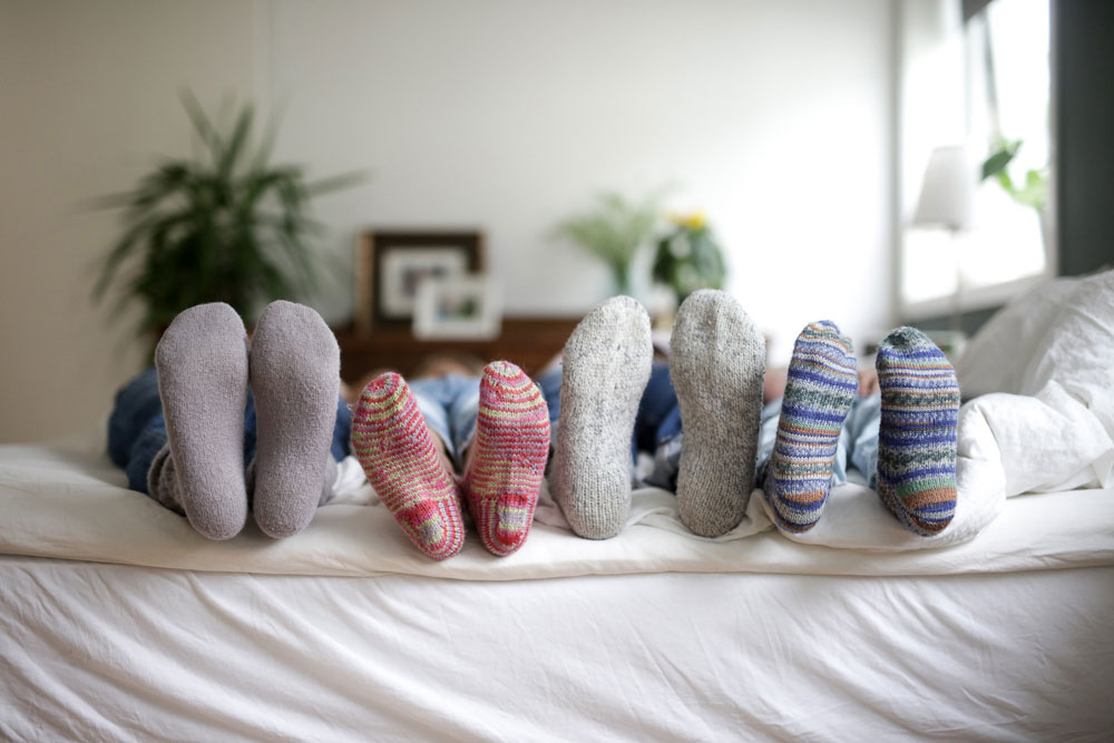 Tykke sokker på fire par ben hos en småbarnsfamilie som ligger på tvers i en dobbeltseng for å illustrere tiltak for å spare strøm.